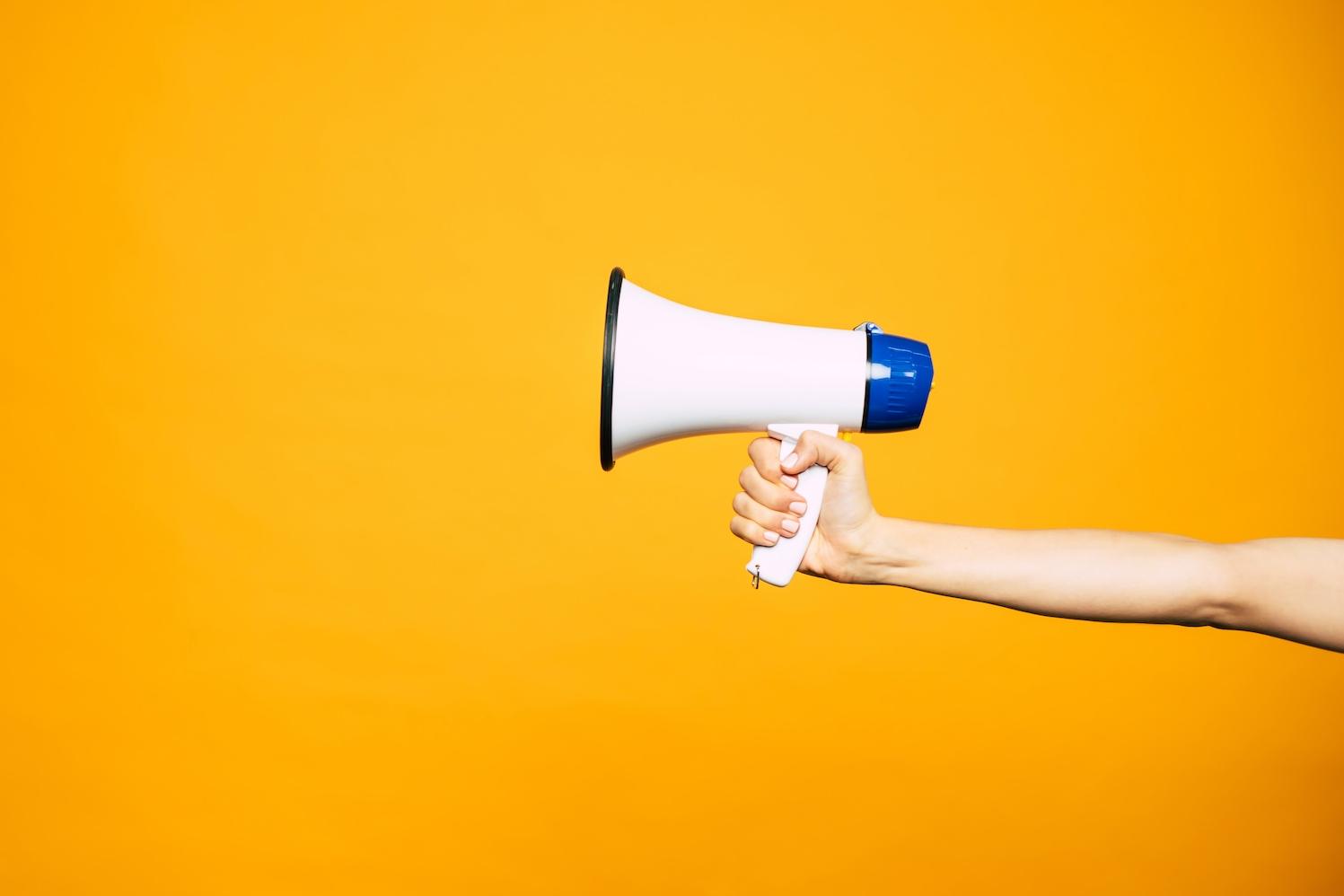 hand holding megaphone against yellow background - the top ESG issues brands should speak out on in 2024