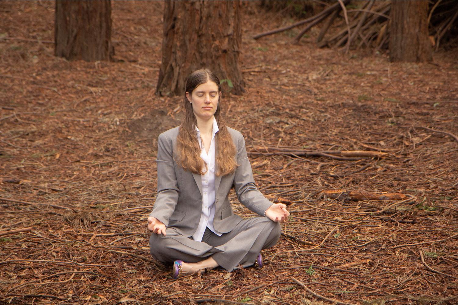 woman meditating in the woods while wearing a business suit 