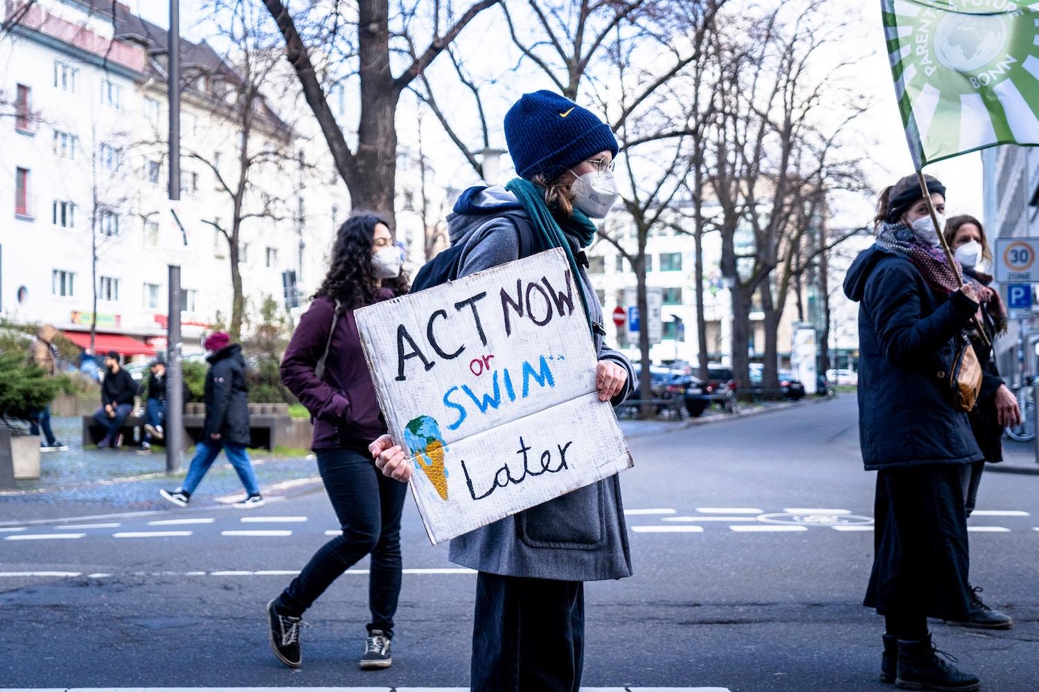 A climate activist holds a sign that states "act now or swim later." 