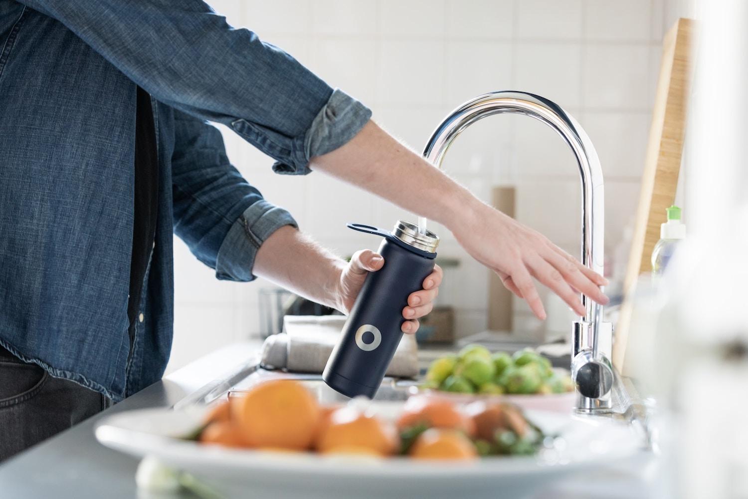 person filling up a reusable water bottle - sustainability behaviors