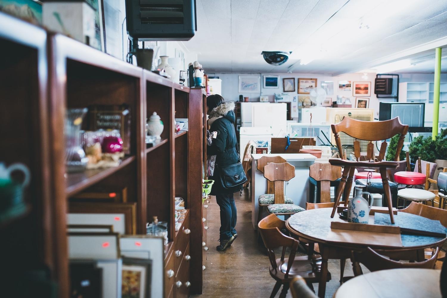 woman in a thrift store surrounded by pre-owned furniture and housewares - shop secondhand