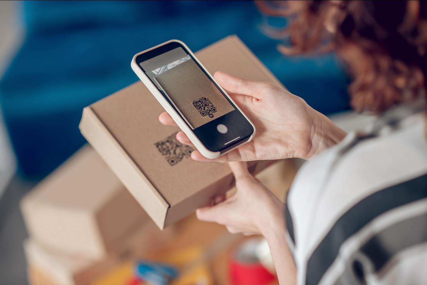 woman scanning QR code on box with phone - QR codes and other 2D barcodes can help brands communicate ESG and sustainability information