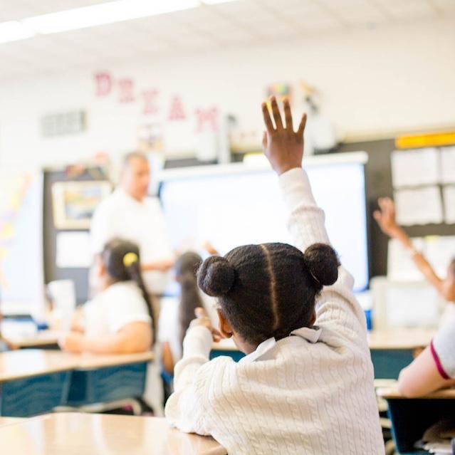 A student raising their hand in a classroom — DonorsChoose