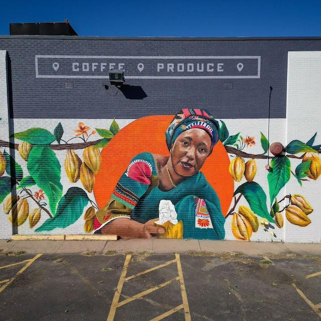 The Denver mural depicting Salamatu Katta in an orange circle surrounded by a cacao tree on the wall of Leevers Locavore in Denver, Colorado— Fairtrade farmers