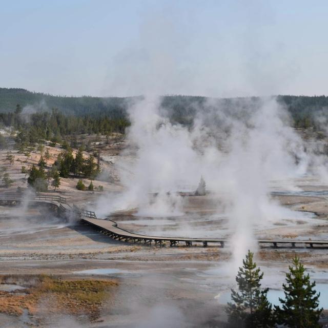 Steam rises up from a geyser basin, displaying of geothermal energy.