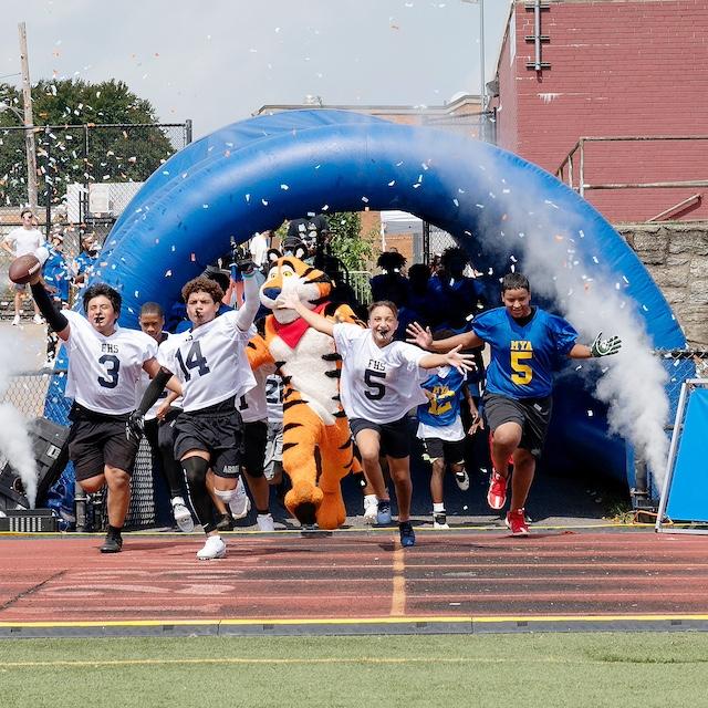 Students run onto a football field with Tony the Tiger as part of Mission Tiger. 