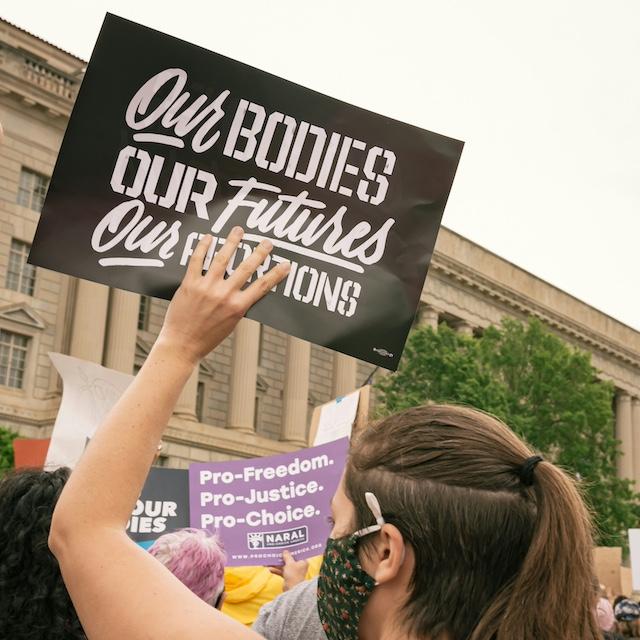 An attendee of a reproductive rights protest holds a sign that reads "Our bodies, our futures, our abortions."