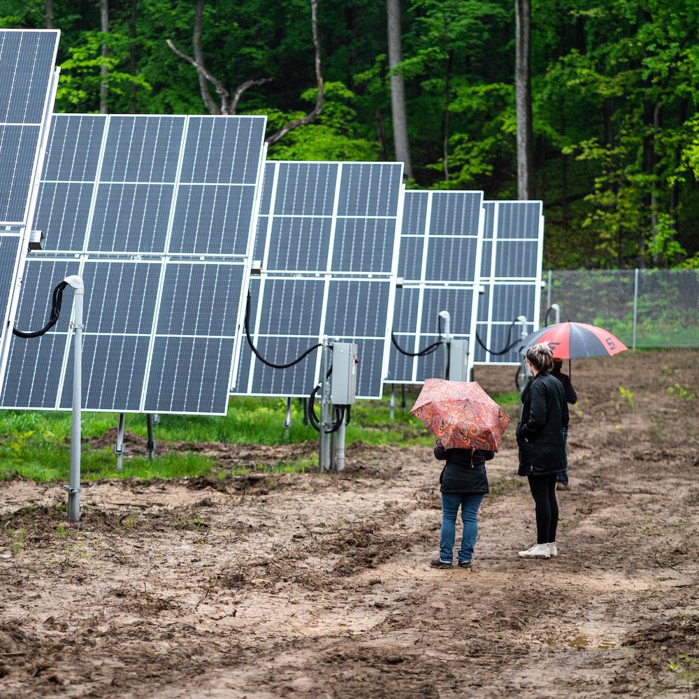 People stand next to a row of solar panels at Lightstar Renewables' project in Saugerties, New York.