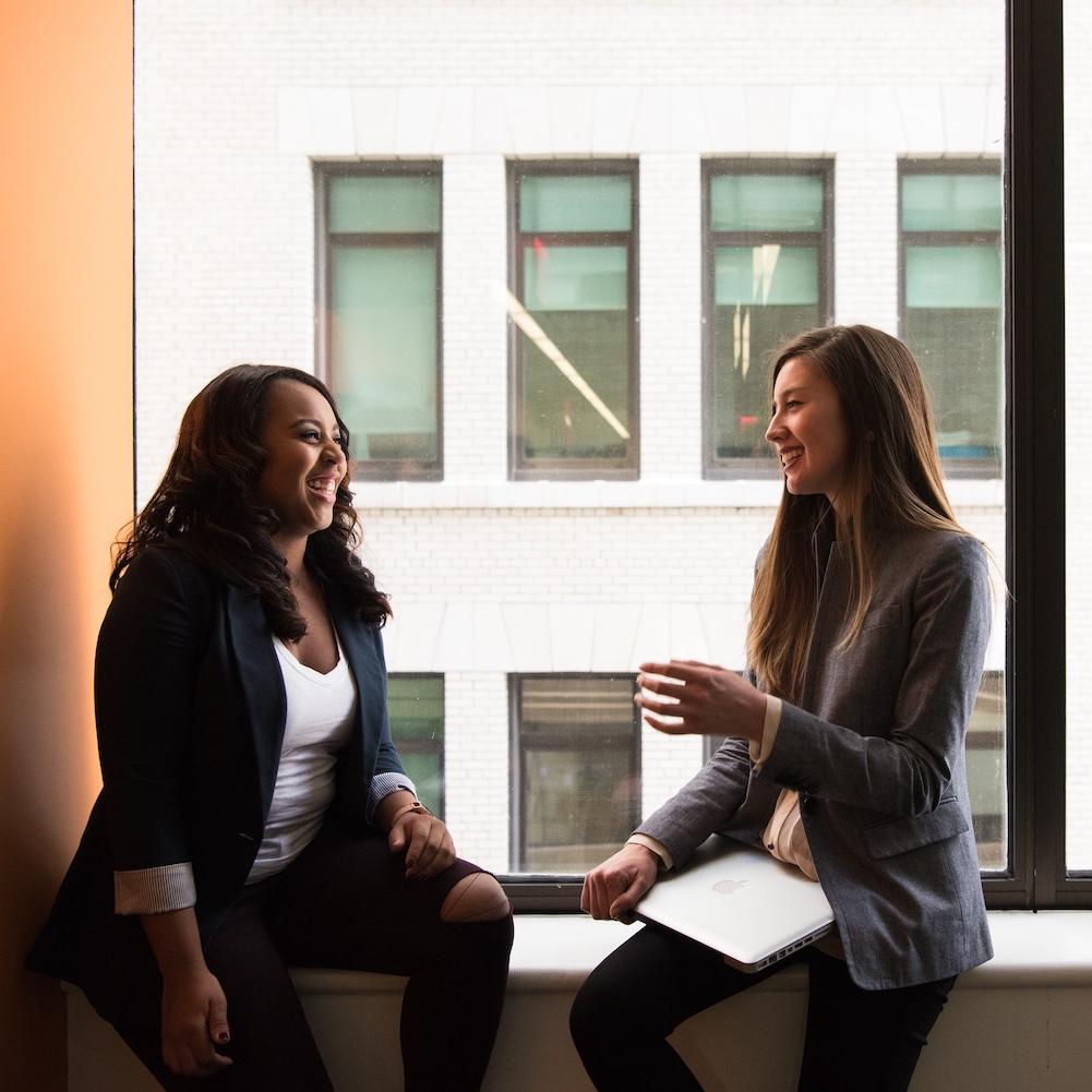 Two women sitting by a window talking. 