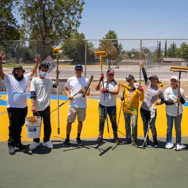 Volunteers paint a mural on a street using cool pavement coating.