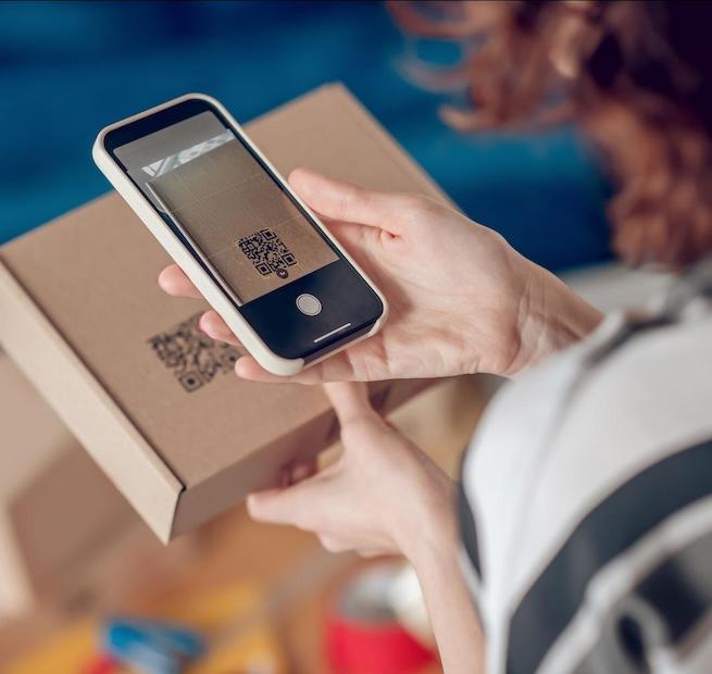woman scanning QR code on box with phone - QR codes and other 2D barcodes can help brands communicate ESG and sustainability information