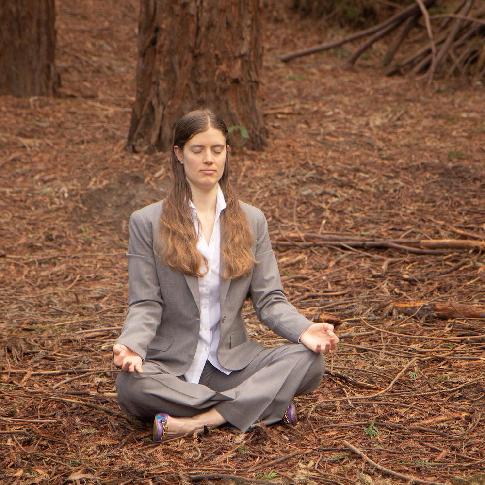 woman meditating in the woods while wearing a business suit 