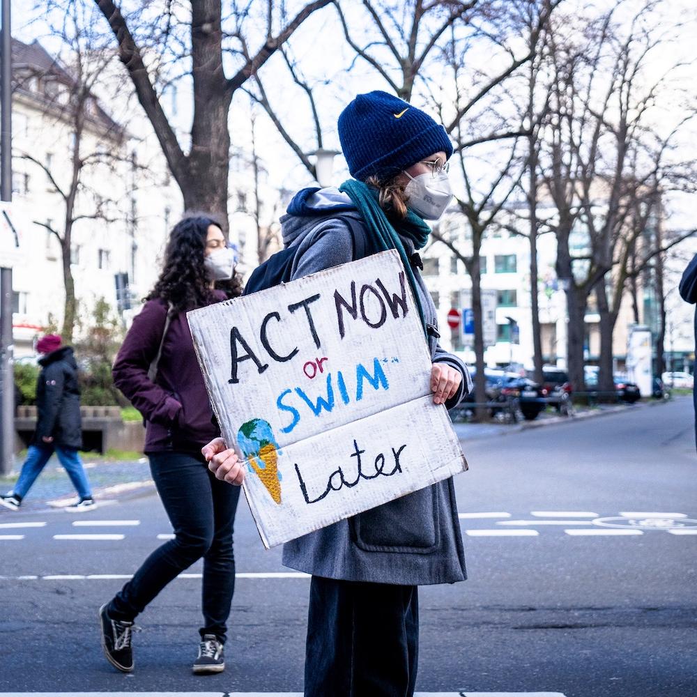 A climate activist holds a sign that states "act now or swim later." 