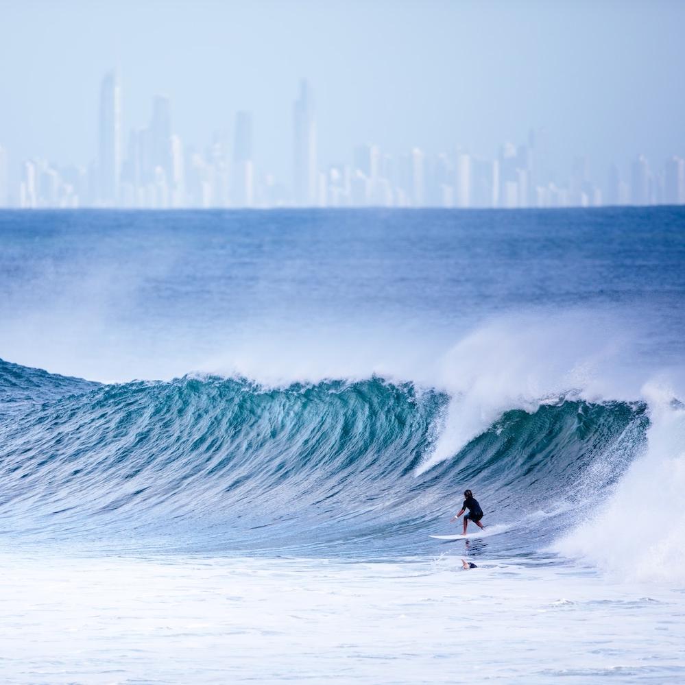 people surfing in the ocean with city skyline in the background - gold coast australia - technology to turn seawater into green hydrogen