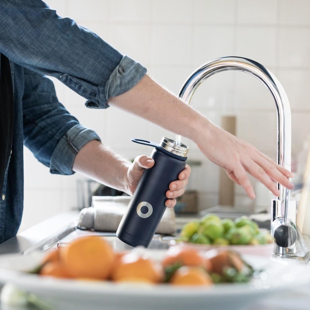 person filling up a reusable water bottle - sustainability behaviors