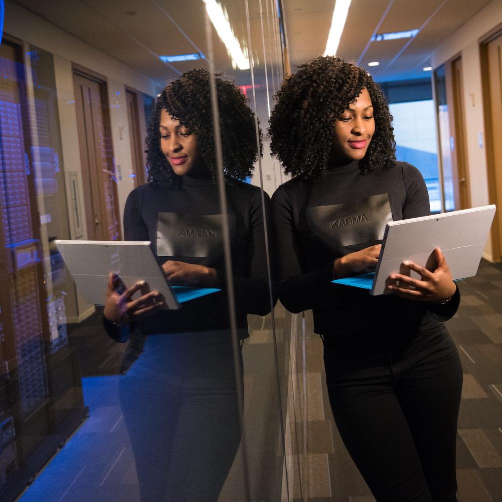 A photo of a woman and her reflection working on a laptop in front of a server room - soft skills for tech leaders